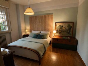 Ein Schlafzimmer mit einem Bett, Nachttischlampen, einem Gemälde und einem Fenster.