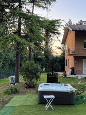 Een bubbelbad in een achtertuin met een huis, bomen en een overdekte barbecue.