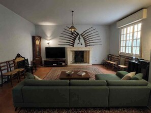 A living room with a green sofa, a fireplace, a television, and a wall-mounted decorative piece. - Charming Villa with a Hot Tub in a Pine Forest (Talacchio)
