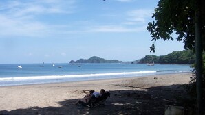 A beach with people sitting on a chair, a sandy shore, and boats in the water. - Luxury 2nd Floor Condo - 5 Minute Walk to Award-Winning Playa Hermosa Beach (Playa Hermosa)