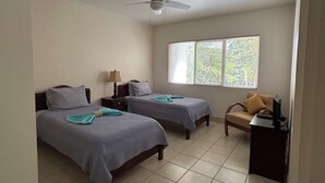A hotel room with two beds, a desk, a chair, a ceiling fan, and a window with blinds. - Luxury 2nd Floor Condo - 5 Minute Walk to Award-Winning Playa Hermosa Beach (Playa Hermosa)
