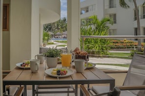 Een balkon met een tafel, ontbijtartikelen, uitzicht op een resortzwembad en omliggend groen.