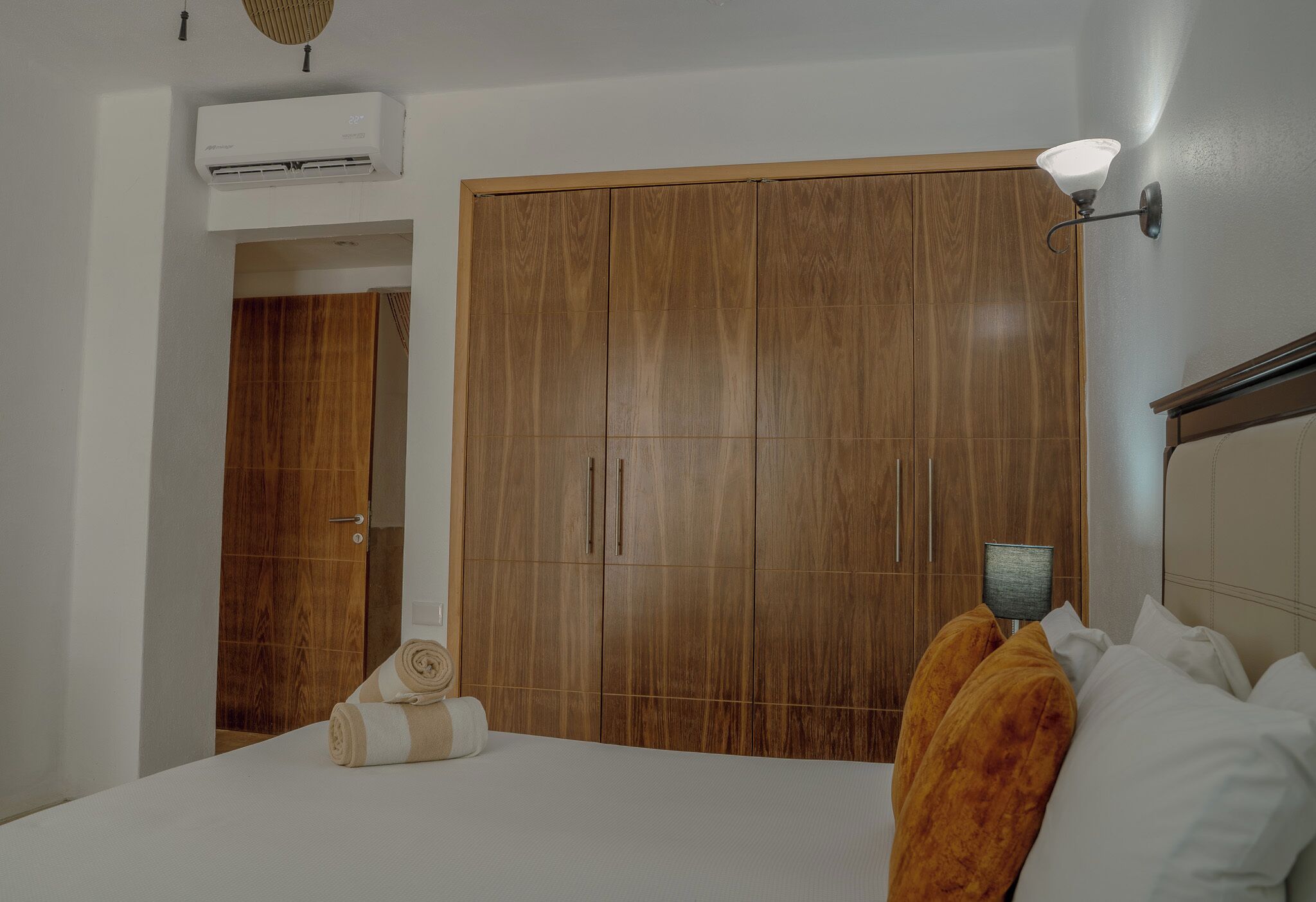 Ein Schlafzimmer mit großem Kleiderschrank, einem Bett mit weißer Bettwäsche und einem Nachttisch mit Lampe.