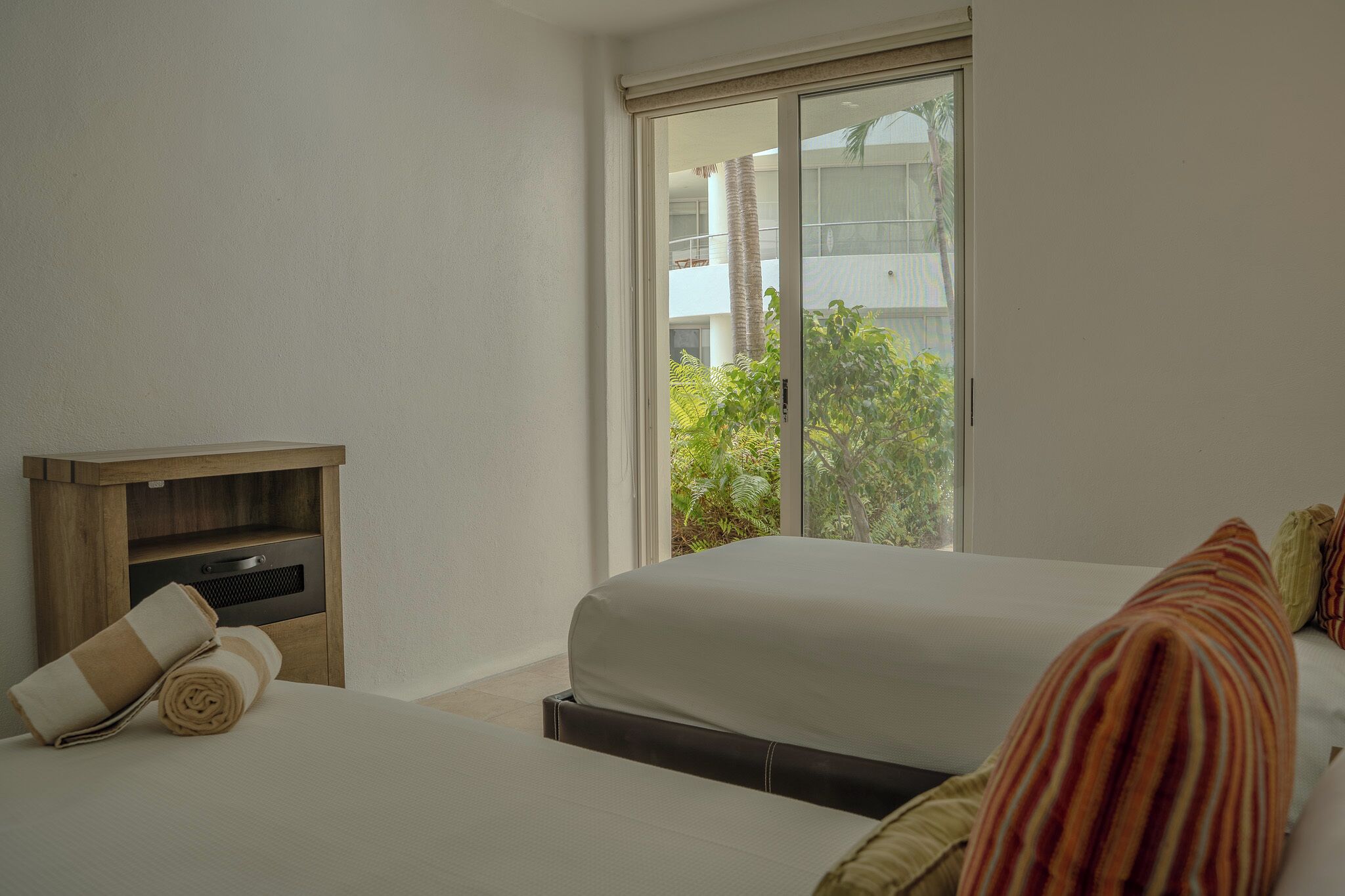 Ein Hotelzimmer mit Bett, einem kleinen Holzschrank und einem Fenster mit Blick auf Grünfläche.