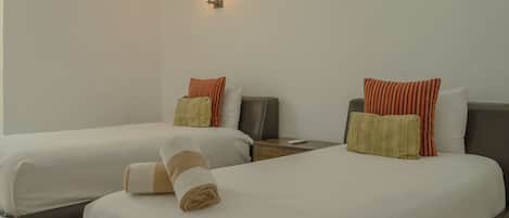 A hotel room with two beds, each with a pillow and a rolled towel.