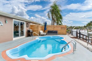 Ein Schwimmbecken mit Holzterrasse, Grill und Liegestuhl.