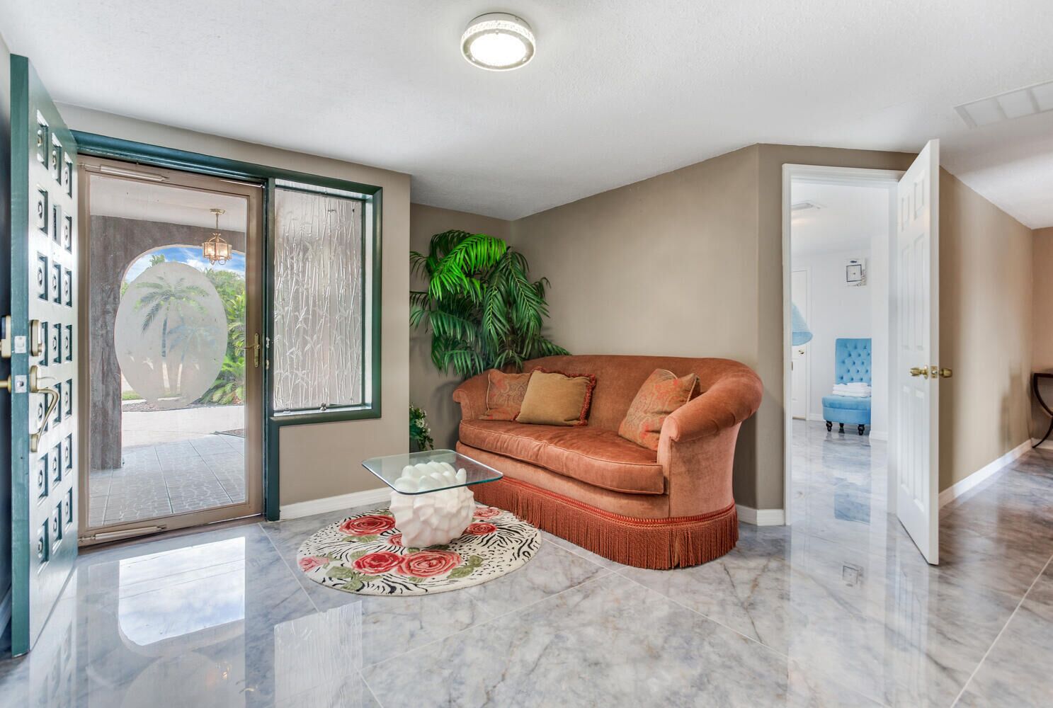 Ein Wohnzimmer mit einer Couch, einem Glastisch, einem gemusterten Teppich und einer Tür zu einem anderen Raum.