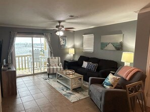 Ein Wohnzimmer mit Sofa, Sessel, Couchtisch und Deckenventilator. Durch eine Schiebetür bietet sich Meerblick.