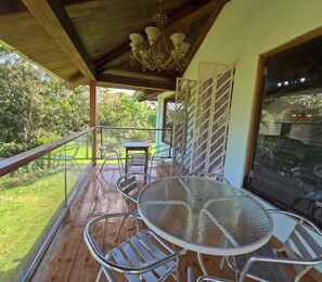 Un espace extérieur abrité, doté d’une table ronde et de chaises en métal, d’un plafond en bois et offrant une vue sur la verdure.