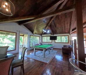 A spacious room with a pool table, comfortable seating, and large windows offering natural light and views.