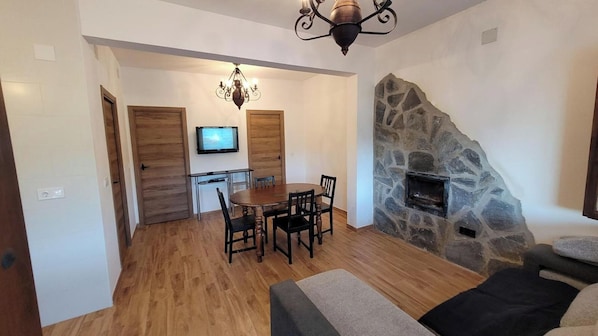 A dining area with a wooden table and chairs, a television mounted on the wall, and a stone fireplace. - Finca 3R Vélez-Málaga by Ruralidays (Málaga)