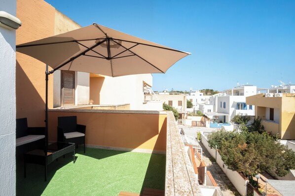 A rooftop terrace with a table and chairs, a large umbrella, and a view of surrounding buildings. - VILLA 200 METERS FROM THE BEACH, GARDEN WITH GAZEBO AND BARBECUE AREA, PARKING SPACE INCLUDED (San Vito Lo Capo)