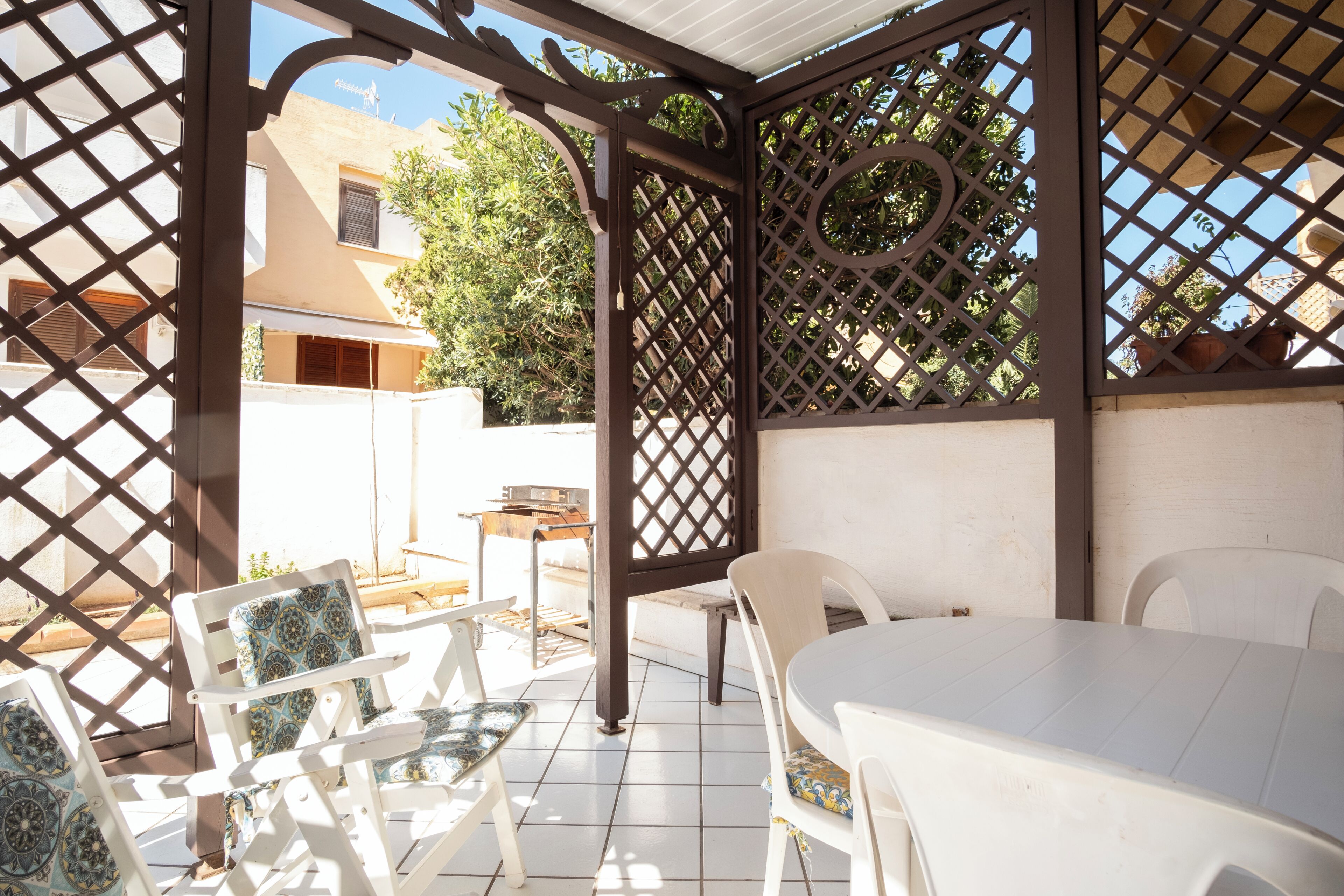 An outdoor patio with a white table and chairs, a grill, and a lattice structure.