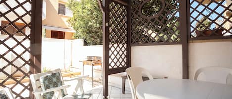 Un patio al aire libre con mesa y sillas blancas, una parrilla y una estructura de celosía.