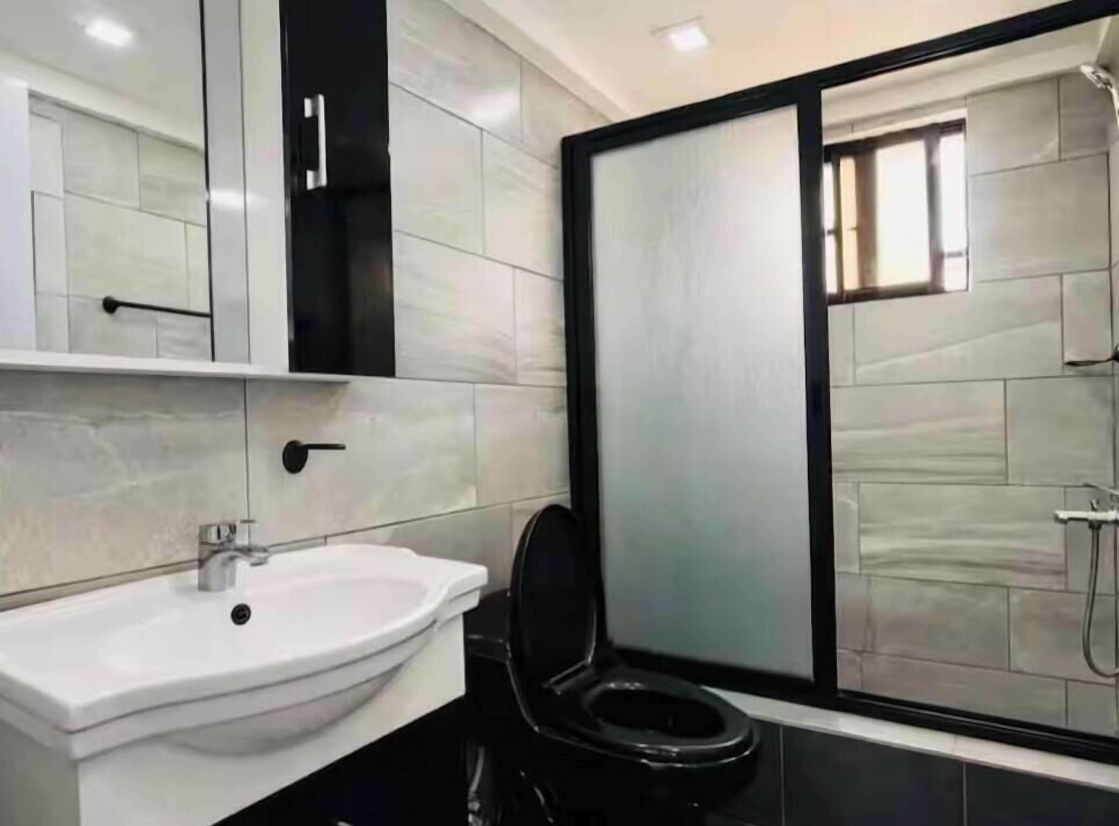 A bathroom with a white sink, black toilet, and a glass shower enclosure.