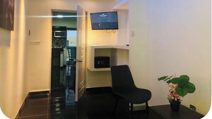Una habitación moderna con una televisión de pantalla plana montada en la pared, una silla de oficina negra, una pequeña planta en maceta y una puerta que da a otra habitación.