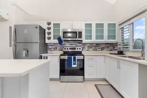 A modern kitchen with white cabinetry, stainless steel appliances, and a large window providing natural light. - Richmond Estate 3rd floor condo~ Pool~Beach Access (Claremont)
