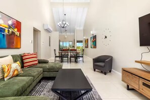 Ein modernes Wohnzimmer mit einer Couch, einem Couchtisch, einem Fernseher und einem Essbereich mit Stühlen und einem Tisch.