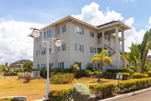 A multi-story residential building with a balcony on the second floor, surrounded by well-maintained landscaping and a clear sky. - Richmond Estate 3rd floor condo~ Pool~Beach Access (Claremont)