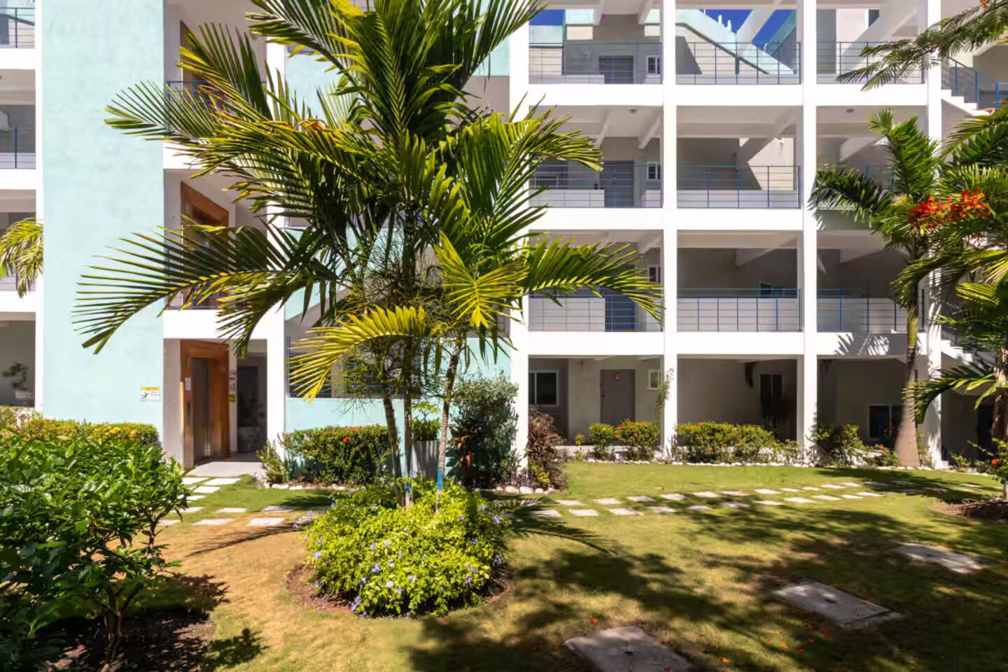 A multi-story building with balconies, surrounded by well-maintained gardens and palm trees.