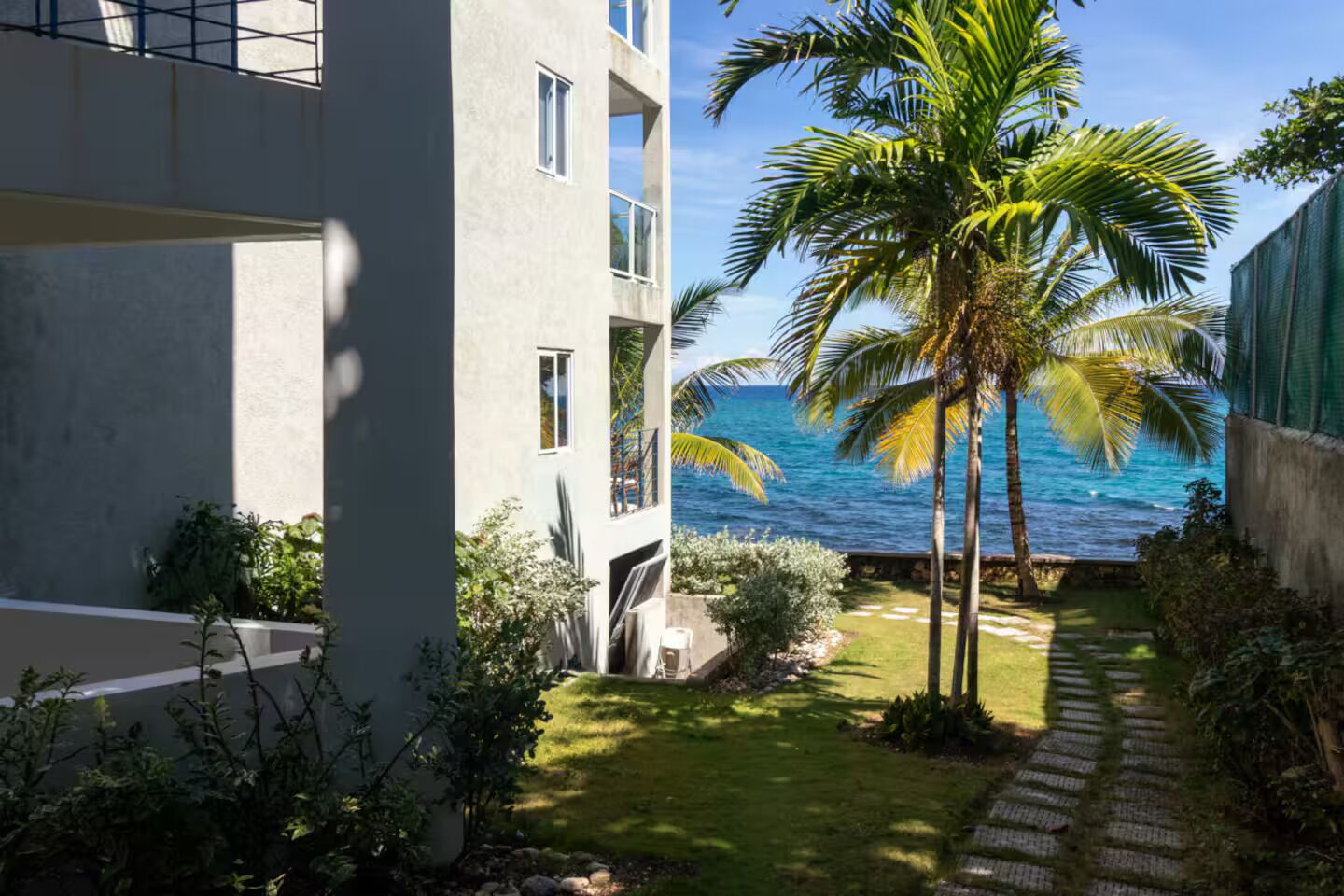 A modern building with a balcony overlooking a palm tree and the ocean.