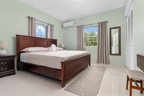 A neatly arranged bedroom with a wooden bed, a bedside table, a chair, and a window with curtains. - 2Brm Condo Tower Isle~Gated~15 mins to Ocho Rios (Boscobel)