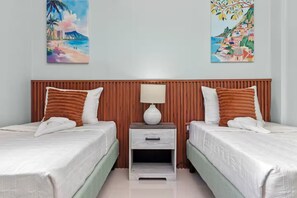 Ein Hotelzimmer mit zwei Betten, einem Holzkopfstück, einem Nachttisch mit Lampe sowie zwei Bildern an der Wand.