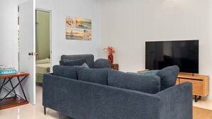 Moderni olohuone, jossa on harmaa sohva, litteänäyttöinen televisio ja pieni sivupöytä.