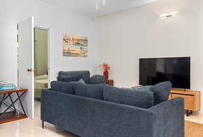 Ein modernes Wohnzimmer mit einem grauen Sofa, einem Flachbildfernseher und einem kleinen Beistelltisch.
