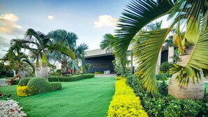 Ein gepflegter Garten mit ordentlich gestutzten Rasenflächen, Palmen und einem Gebäude mit der Aufschrift 'RADISIAC BEACH CLUB'.