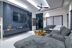 A modern living room with a grey sofa, a glass coffee table, and a flat-screen TV mounted on a dark wall. - NEW~ Pool Access 3BR •Gated • Walk to the Beach (St. Ann Parish)
