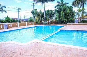 Piscina com deck ladrilhado, cercada por palmeiras e céu claro.
