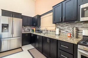 A modern kitchen with dark cabinets, stainless steel appliances, and a granite countertop. - 8BedRm Oasis ~Draxhall ~Pool ~Gym ~PlyGrnd ~Tennis (Saint Ann's Bay)