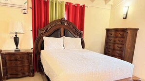 Ein ordentlich bezogenes Bett mit einem Holzkopfteil, ein Nachttisch mit einer Lampe und eine Kommode aus Holz mit Schubladen.