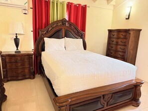 A neatly made bed with a wooden headboard, a nightstand with a lamp, and a wooden dresser with drawers. - 8BedRm Oasis ~Draxhall ~Pool ~Gym ~PlyGrnd ~Tennis (Saint Ann's Bay)