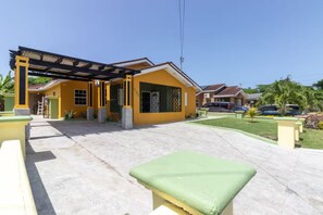 A yellow building with a covered patio area, a paved walkway, and a small lawn. - 3BR Oasis in Drax hall ~ Pool~ Gym ~ Gated ~Tennis (Saint Ann's Bay)