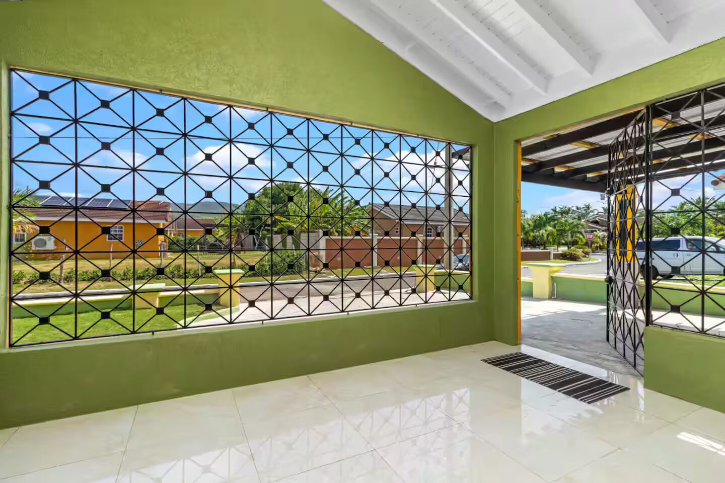 A room with a large window featuring a geometric pattern, a tiled floor, and a view of a residential area.