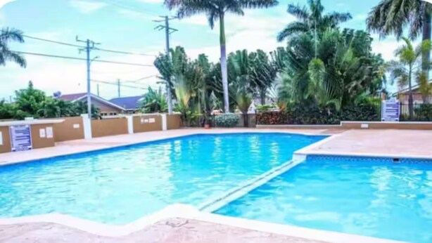 A swimming pool with a tiled deck, surrounded by palm trees and a clear sky. - 3BR Oasis in Drax hall ~ Pool~ Gym ~ Gated ~Tennis (Saint Ann's Bay)