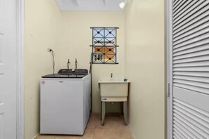 A compact laundry room with a washing machine, a sink, and a window with a geometric pattern. - 3BR Oasis in Drax hall ~ Pool~ Gym ~ Gated ~Tennis (Saint Ann's Bay)