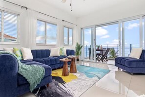 A modern living room with a blue sofa set, a coffee table, and a view of the ocean through large windows. - Blue Serenity ~ Oceanfront Penthouse ~Tower Isle (Tower Isle)
