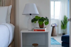 Un comodino bianco con una lampada bianca, una pianta in vaso e un libro.