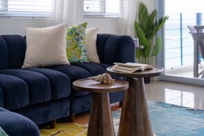 A living room with a dark blue sofa, a round wooden coffee table, and a potted plant. - Blue Serenity ~ Oceanfront Penthouse ~Tower Isle (Tower Isle)