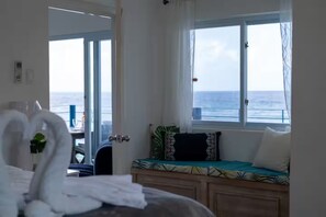 Une chambre avec un lit, une fenêtre donnant sur la mer et un coin salon avec des coussins.