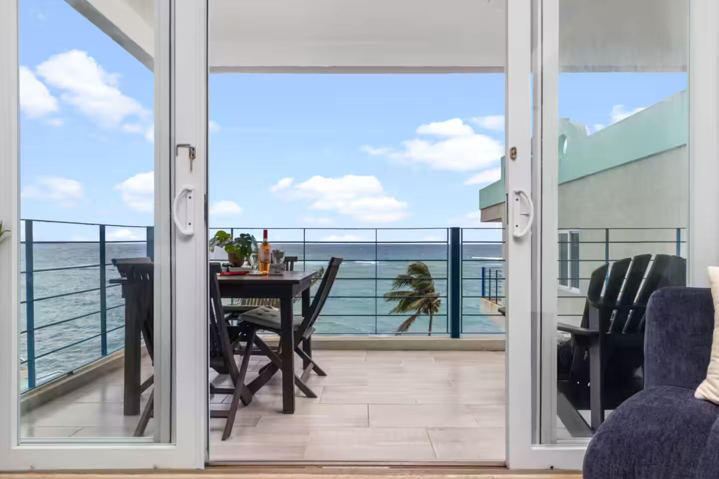 A balcony with a view of the sea, a table with chairs, and a chair in the foreground.