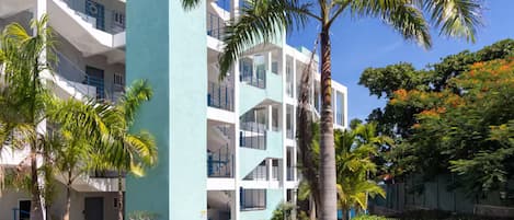 A multi-story building with balconies, palm trees, and a clear blue sky.