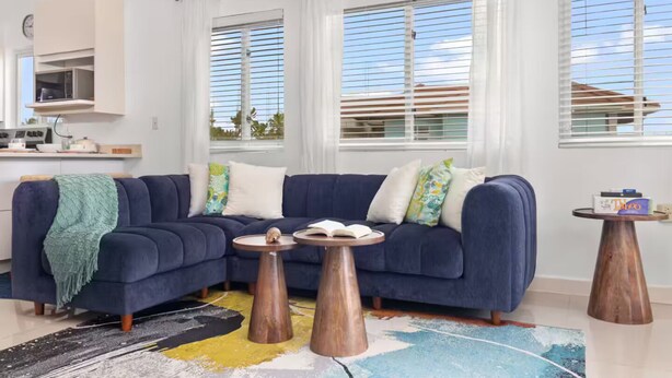 Ein modernes Wohnzimmer mit einem dunkelblauen Sofa, zwei Holztischen und einem farbenfrohen abstraktem Teppich.