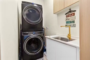 A compact laundry room with a stacked washer and dryer, a sink, and a sign indicating the room's purpose.