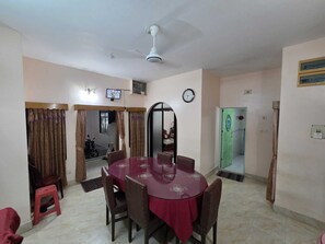 A dining area with a round table, chairs, a ceiling fan, a clock, and a television on the wall.