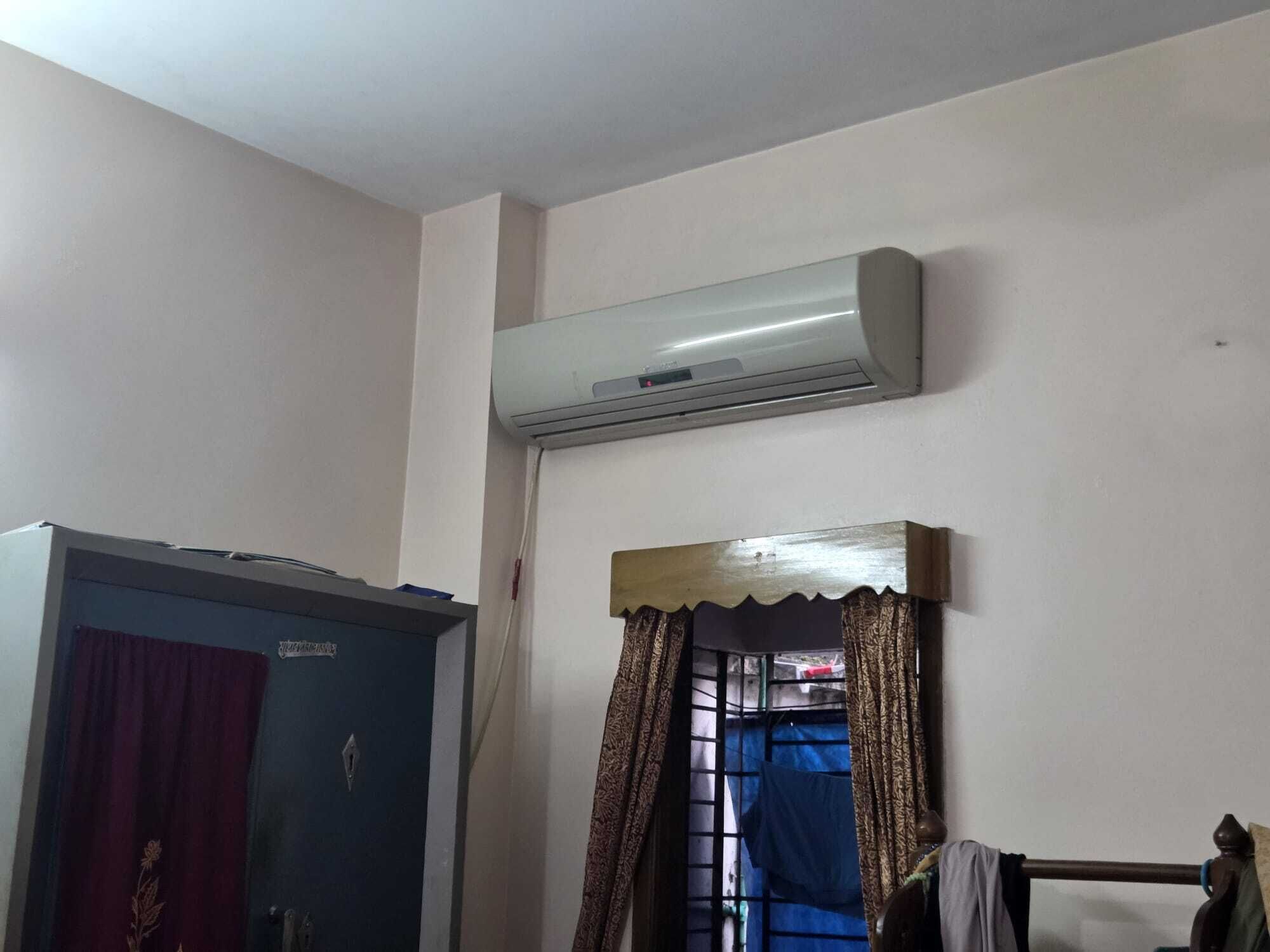 A room with a wardrobe, a window with patterned curtains, and an air conditioning unit mounted on the wall.