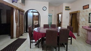 Un'area pranzo con un tavolo rotondo, sedie, una ventola a soffitto, un orologio e una televisione a parete.